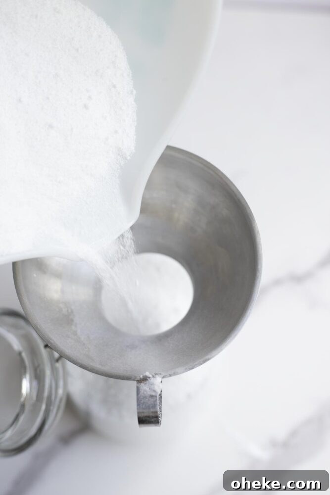 Pouring homemade dishwasher detergent into a glass container with a metal funnel.