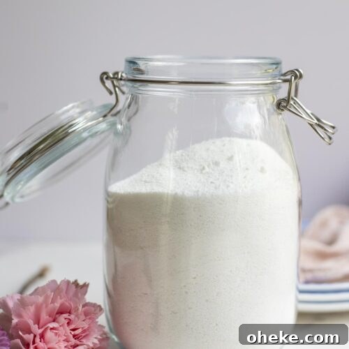 Homemade dishwasher detergent in a swing top jar on a countertop surrounded by flowers.