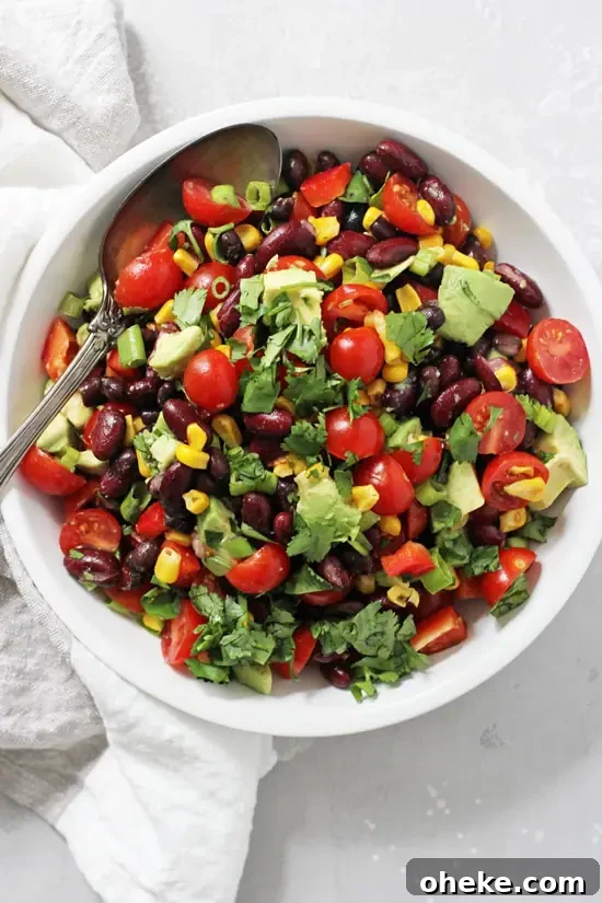 A white bowl filled with Mexican Black Bean Salad with a silver serving spoon in the dish.