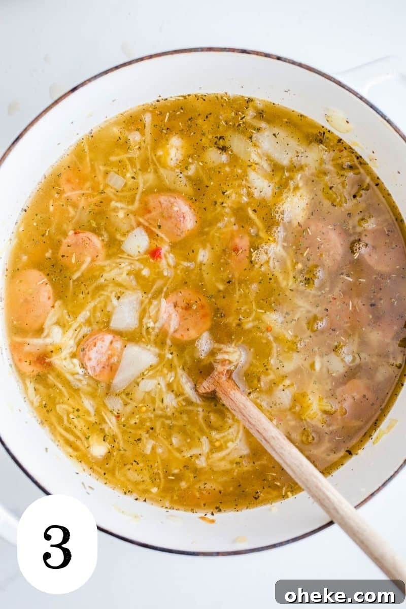 Vegetable broth and sausage in a large white pot.