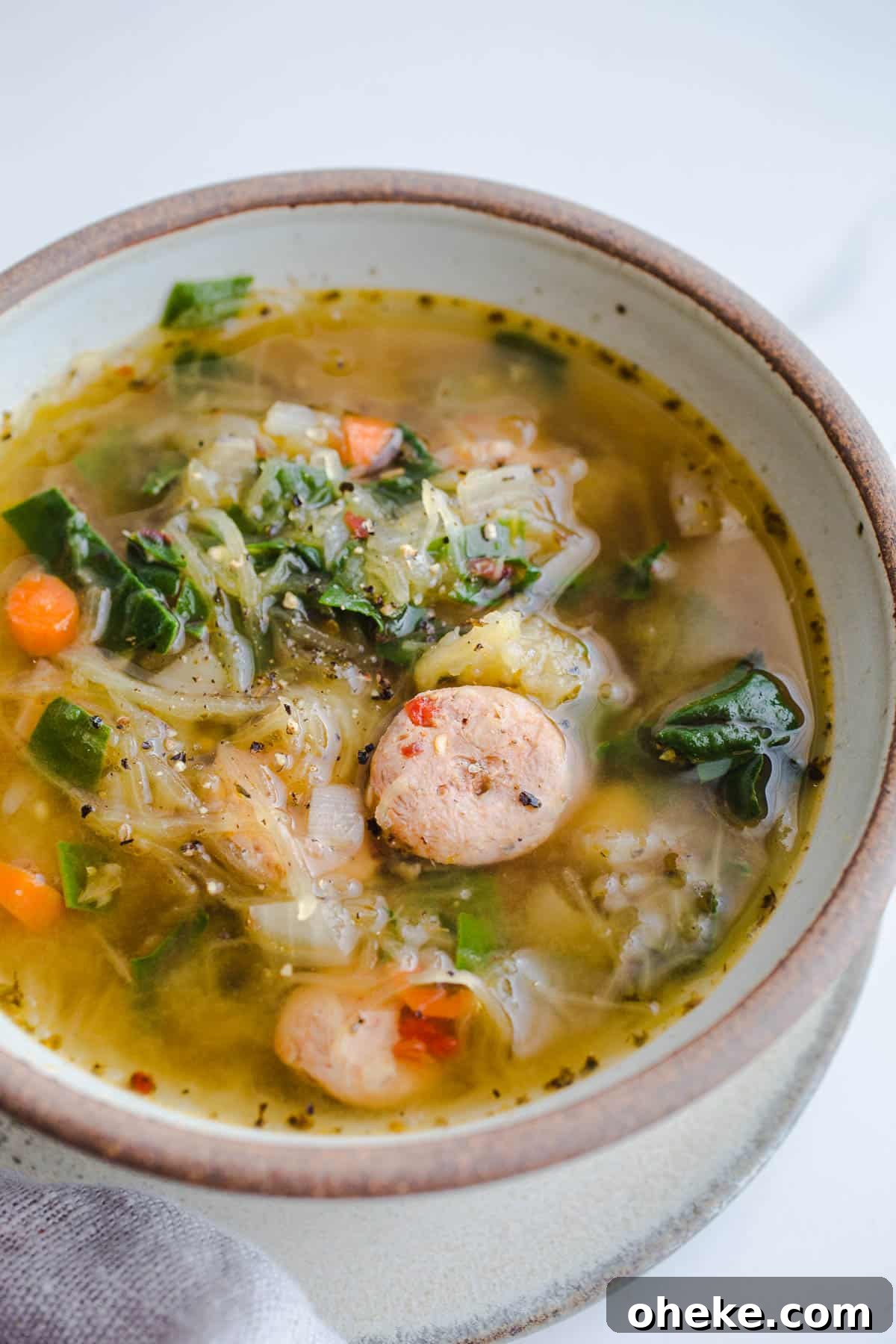Vegetables, chard, and sausage soup in a rustic bowl on a marble surface.