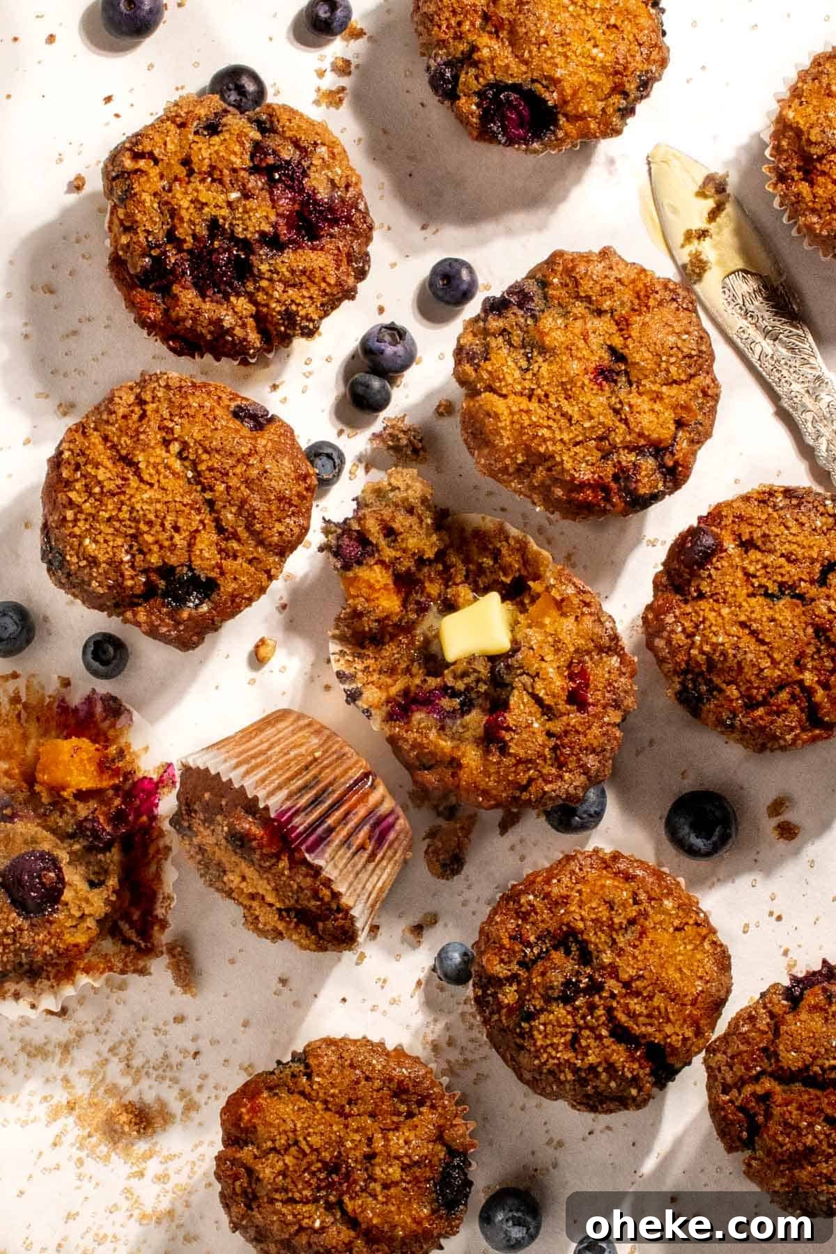 Moist Buttermilk Blueberry Muffins Recipe for Perfect Muffins 2 Buttermilk blueberry muffins spread out on a white background with one muffin sliced open.