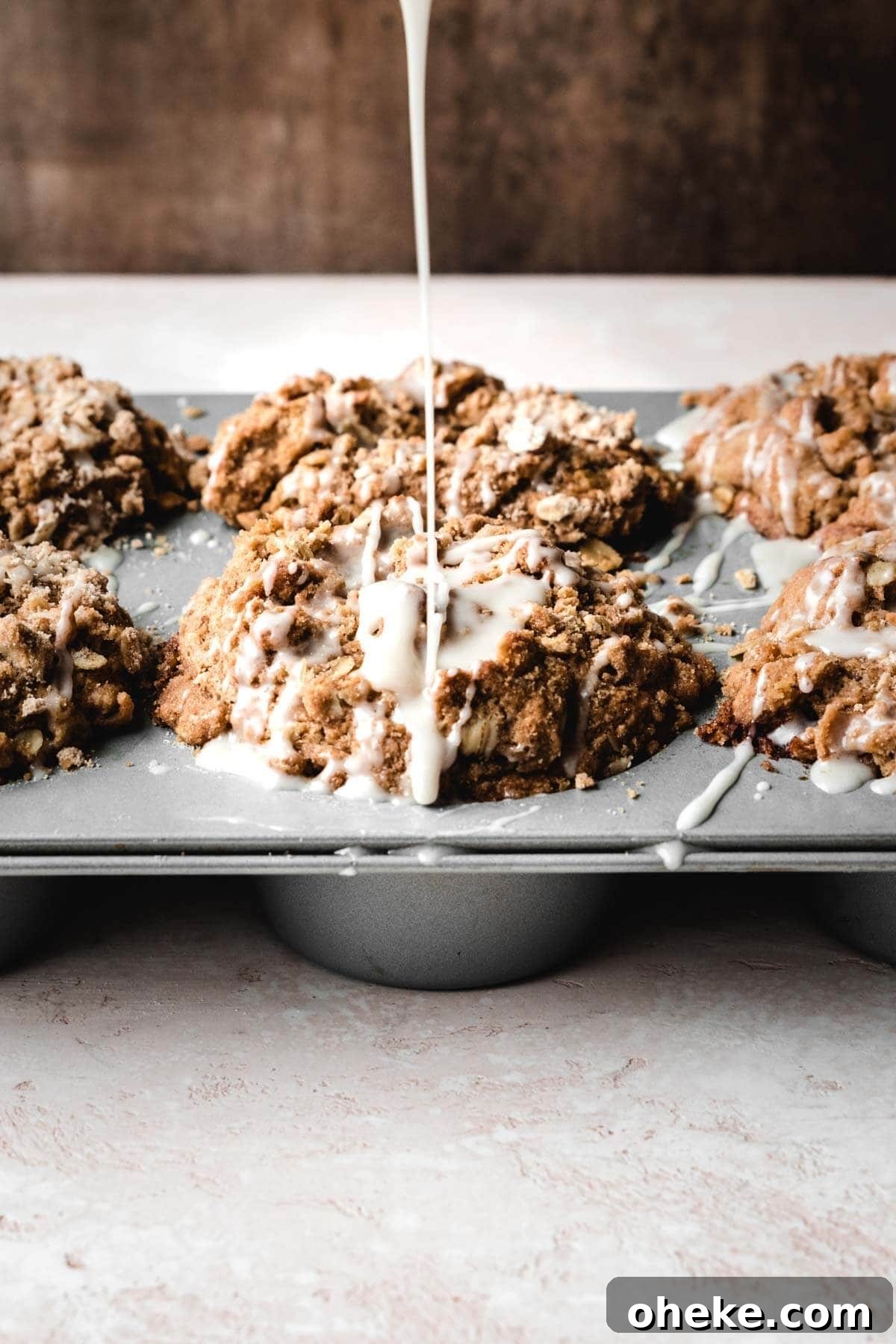 Moist Cinnamon Streusel Muffins Recipe for Perfect Breakfast 4 Glaze being drizzled over cinnamon streusel muffins in a muffin tin.