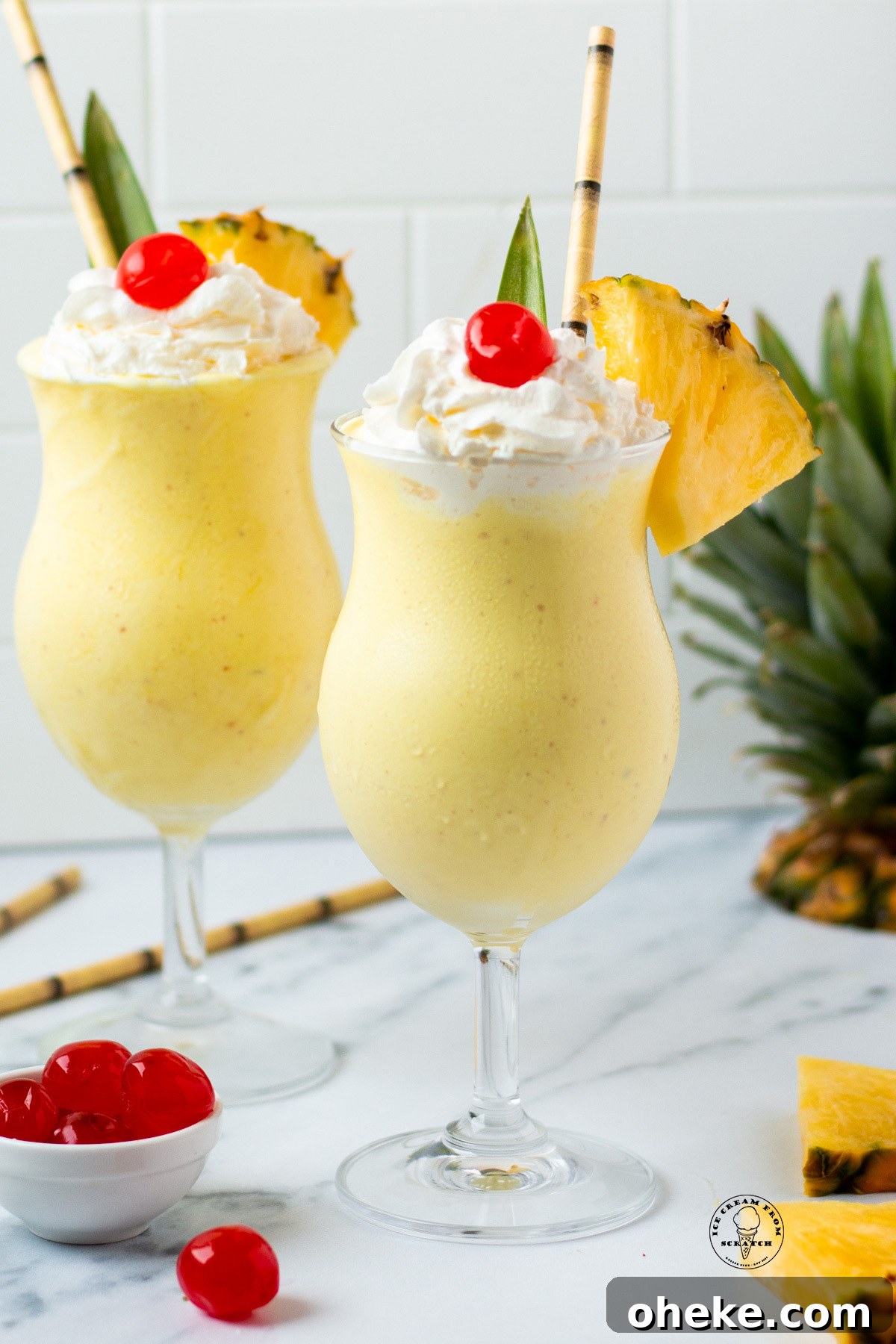 Two pineapple milkshakes in hurricane glasses garnished with a pineapple leaf, whipped cream, cherries, and fresh pineapple wedges.