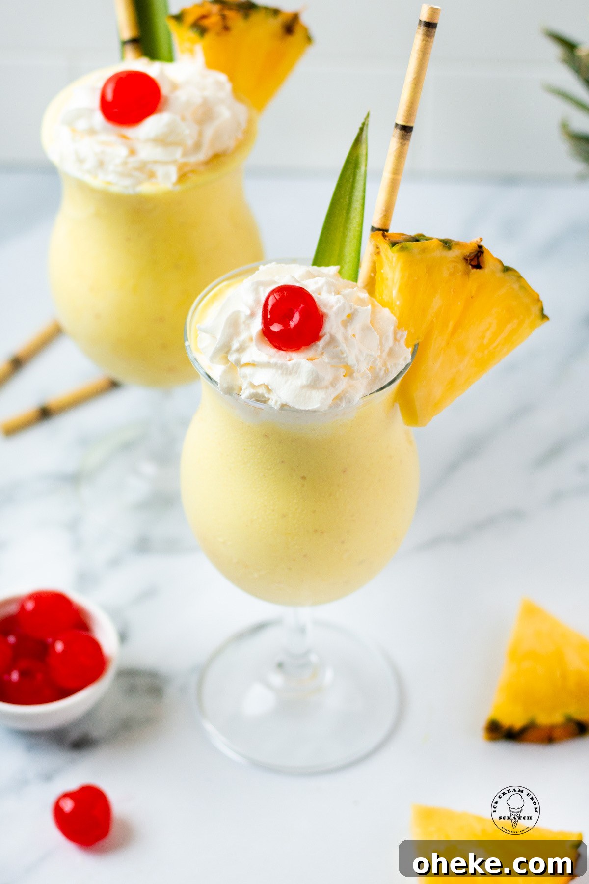 Looking down on two pineapple milkshakes garnished with cherries, pineapple slices, and bamboo straws
