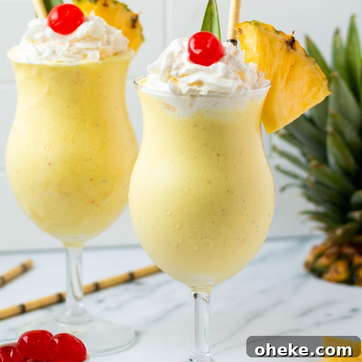 Two pineapple milkshakes in hurricane glasses garnished with a pineapple leaf, whipped cream, cherries, and fresh pineapple wedges.