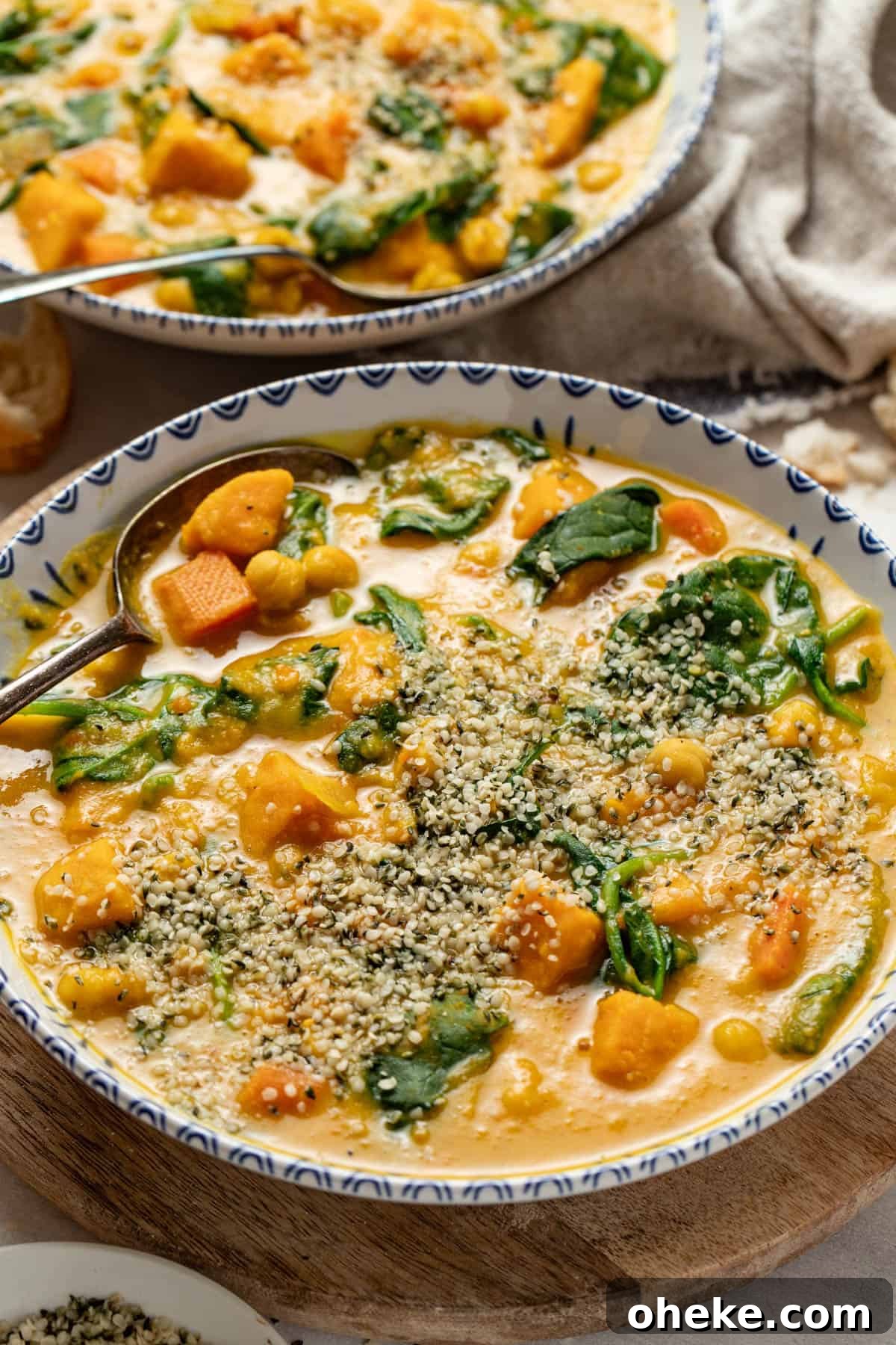 Turmeric Ginger Chickpea Stew to Reduce Inflammation 11 Two bowls of vegetable stew topped with hemp seeds next to a napkin with bread.