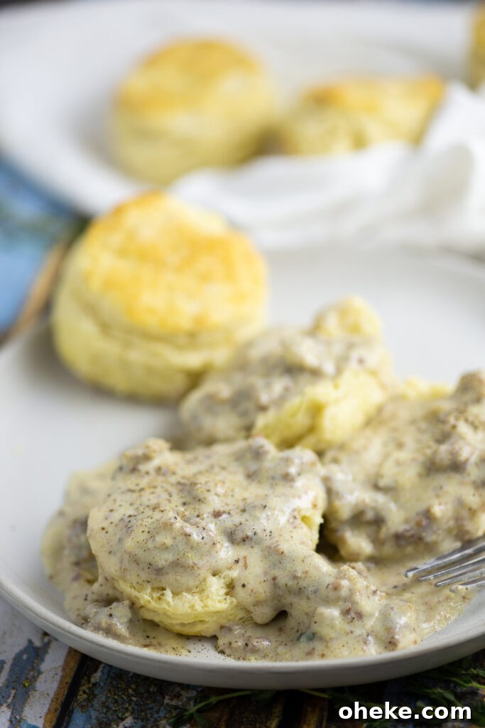 Half a biscuit smothered in sawmill gravy with pork sausage and topped with black pepper with whole biscuits in the background