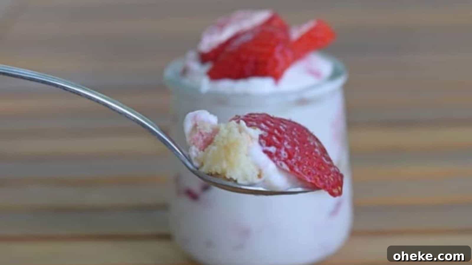 Image shows a spoon holding a scoop of the strawberry lemonade icebox cake with a small jar of the dessert behind it.
