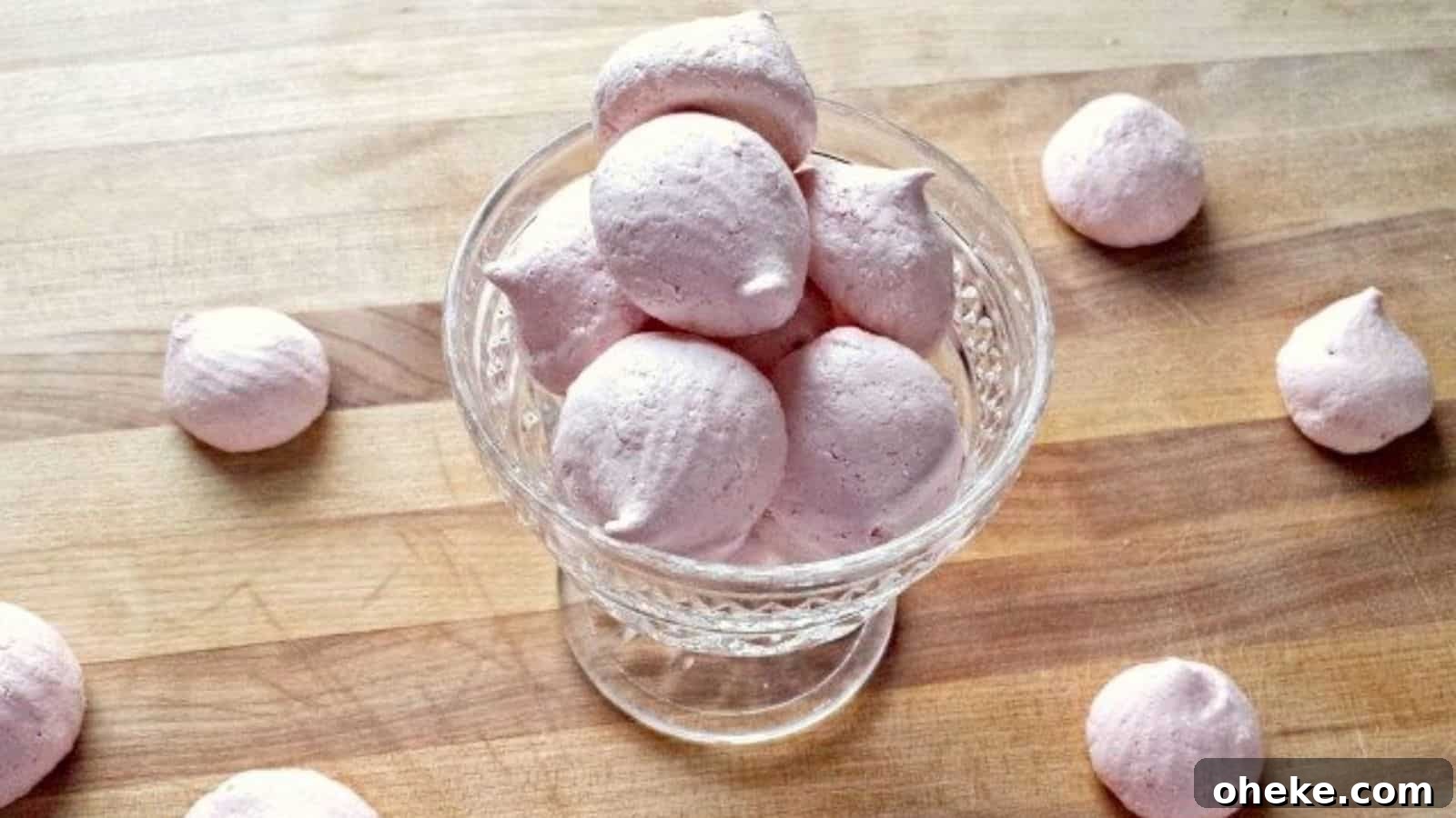Image shows Raspberry Meringues in a glass parfait dish with more surrounding it on a wooden board.
