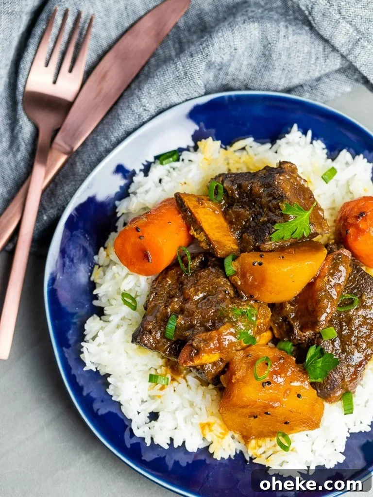 Korean style short ribs with potatoes and carrots with rice on a blue plate with fork and knife