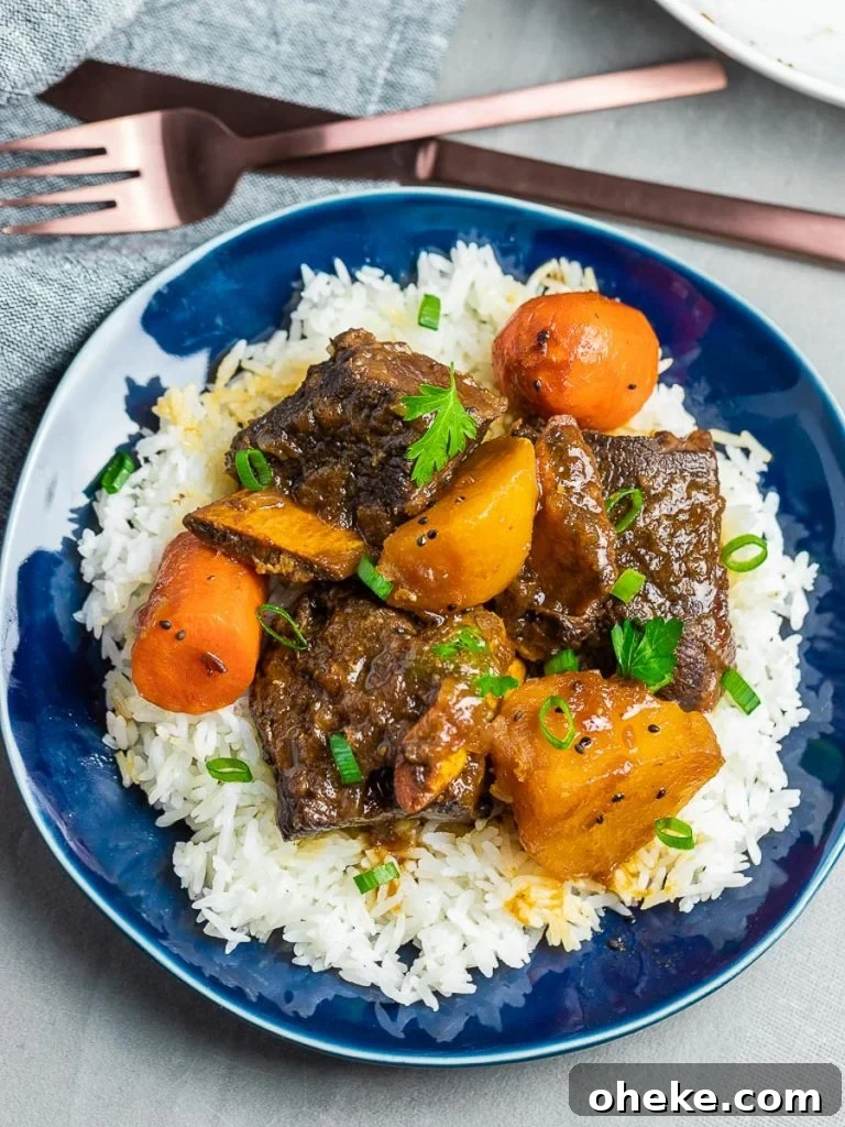 Korean style short ribs with potatoes and carrots with rice on a blue plate next to fork and knife