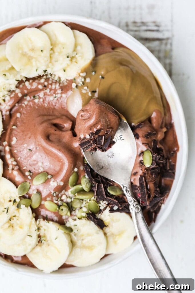Thick Dreamy Chocolate Smoothie Bowl Recipe for Breakfast 2 A spoon taking a bite of a thick chocolate smoothie bowl garnished with banana and seeds.