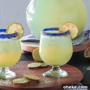 Margarita glasses with lime wedges next to a pitcher.