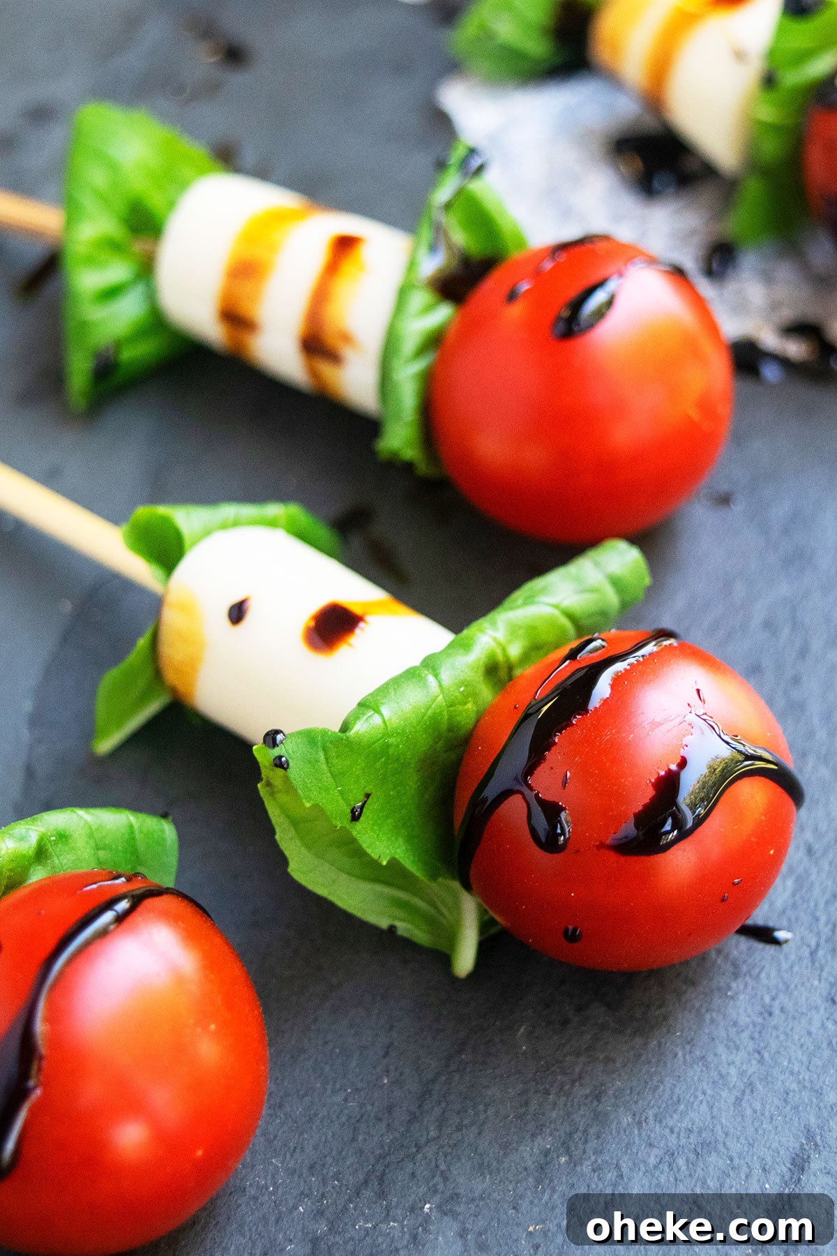 Caprese Skewers on One Pan: Quick Tomato, Basil & Mozzarella Recipe 4 Mini caprese salad kabobs on charcoal gray dish.