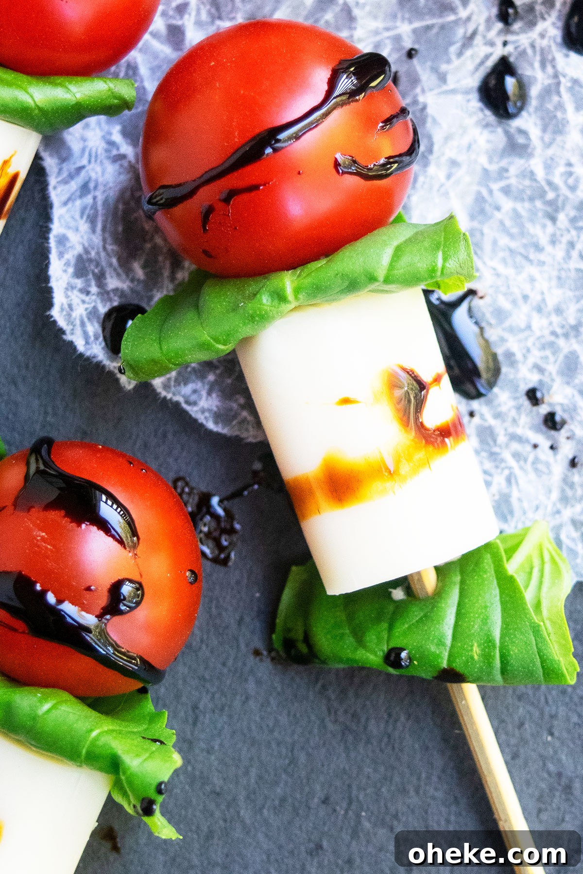 Caprese Skewers on One Pan: Quick Tomato, Basil & Mozzarella Recipe 5 Closeup shot of appetizer on stick on charcoal gray dish with crumpled wax paper.