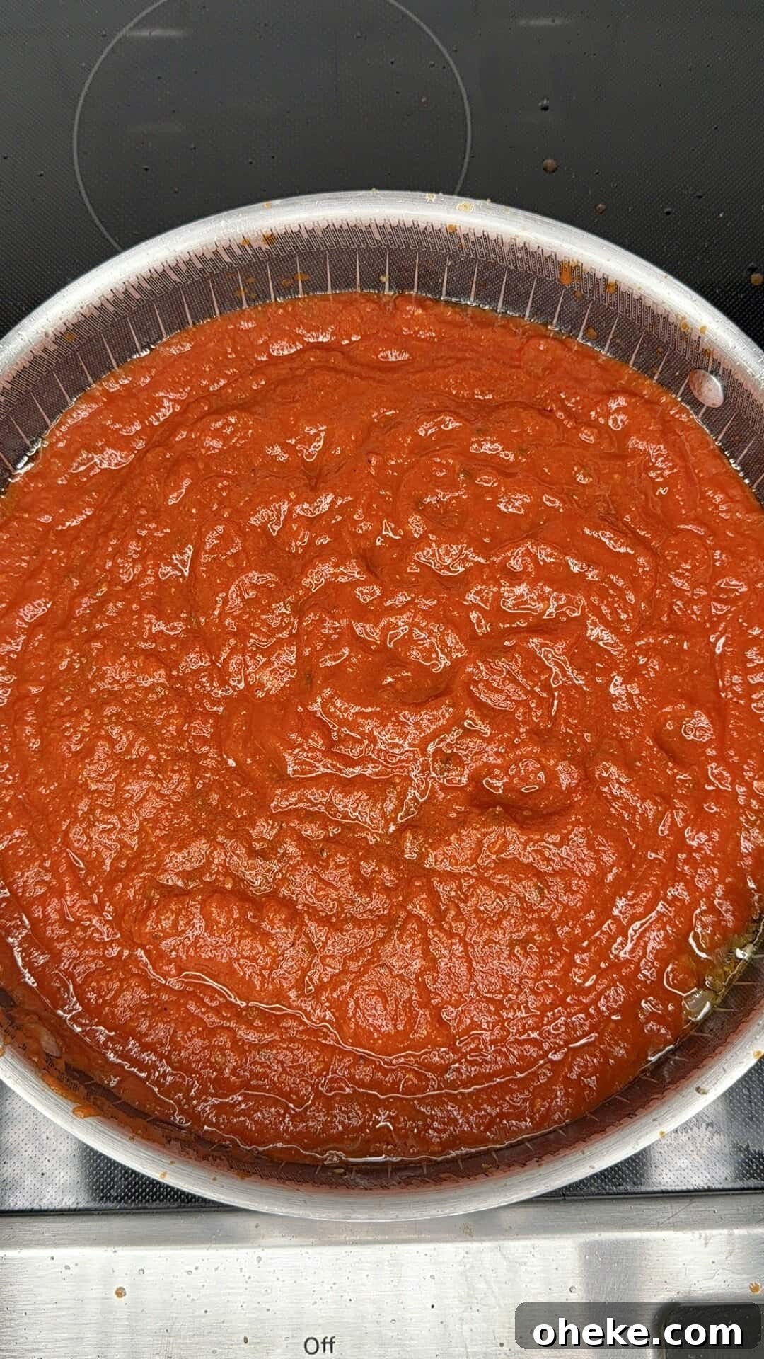 Creamy Italian Baked Spaghetti Recipe — a Tastier Twist on Baked Ziti 5 A large silver pan filled with red tomato sauce sits on a stovetop, with some green herbs visible around the edges of the sauce.