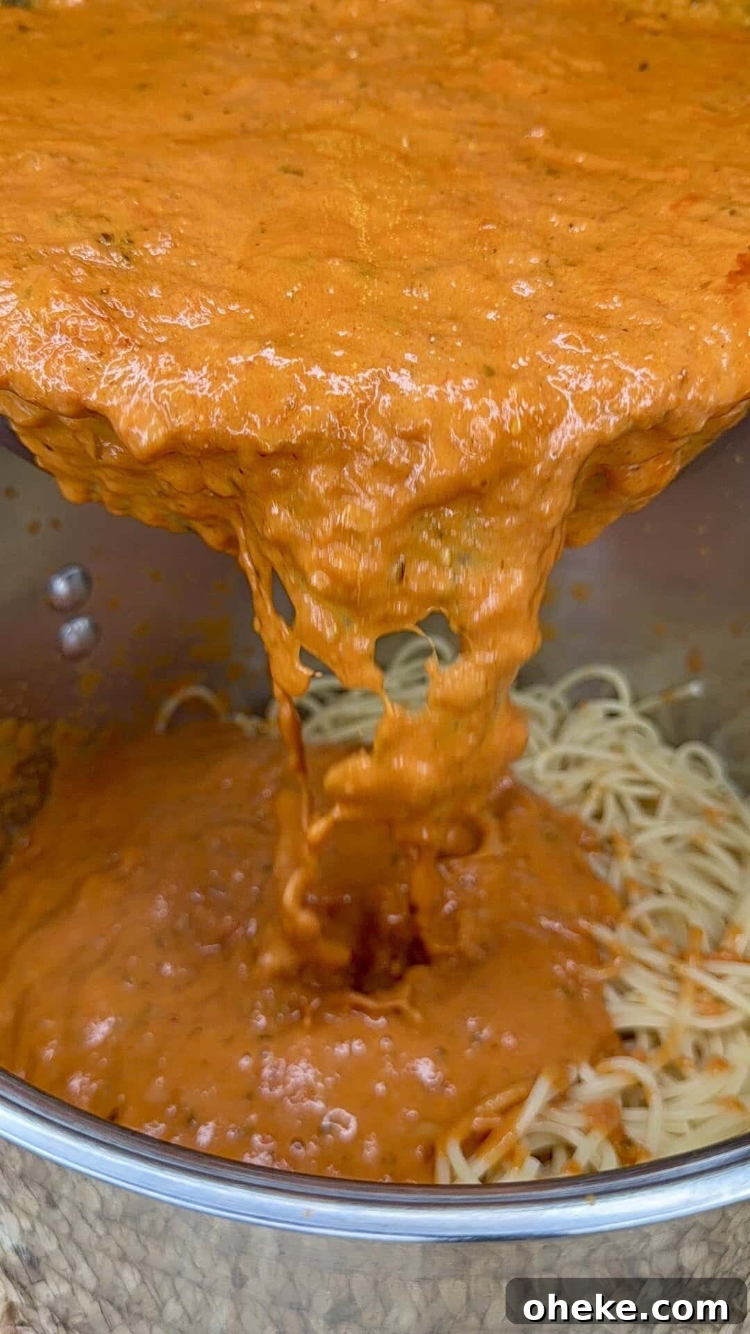 Creamy Italian Baked Spaghetti Recipe — a Tastier Twist on Baked Ziti 8 A close-up view of rich, red tomato sauce being poured over a pot of cooked spaghetti noodles. The sauce is thick and creamy, covering the pasta as it flows from the pot above.