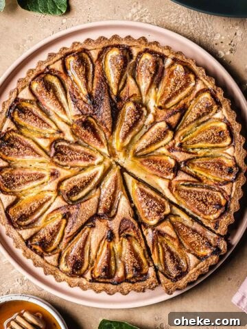 A baked tarte aux figues with a slice cut out, with fig leaves and honey nearby.