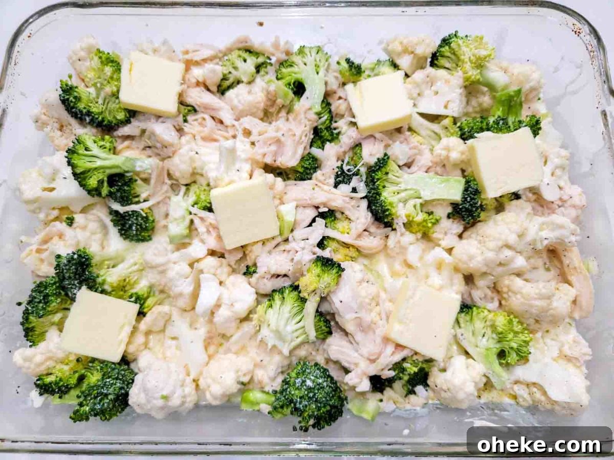 chicken broccoli cauliflower topped with butter pats in a baking dish.