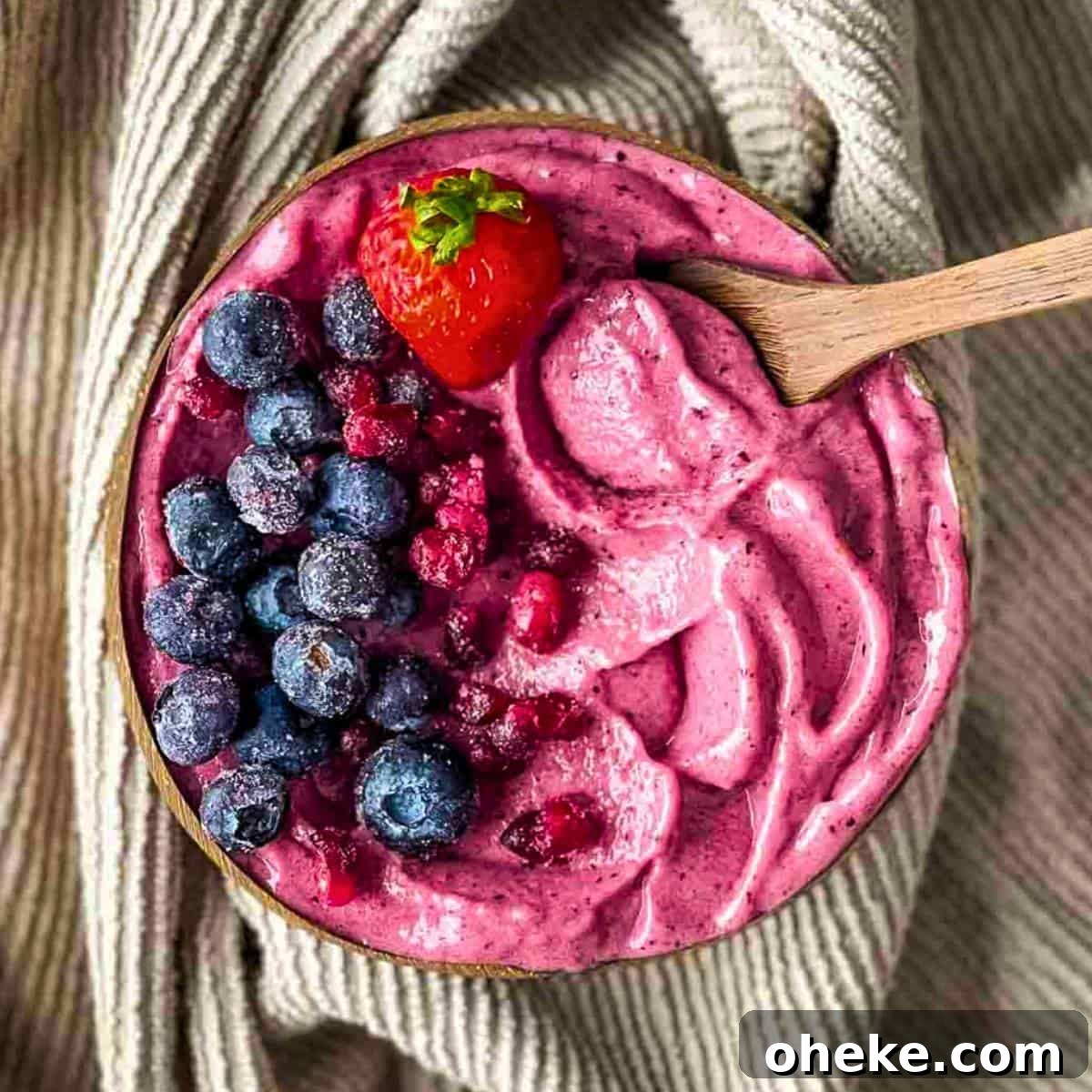 Thick & Creamy Smoothie Bowl Recipe for Spoonable Breakfast 2 A wooden spoon scooping a vibrant, super thick smoothie bowl filled with colorful fruit toppings from an eco-friendly brown coconut bowl.
