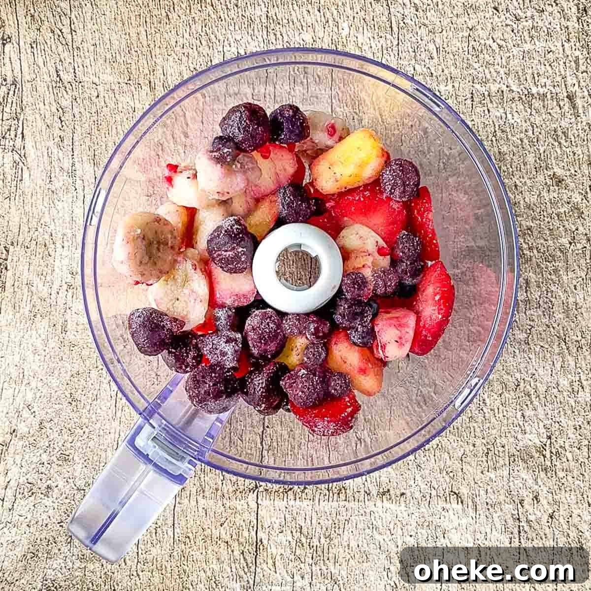 Thick & Creamy Smoothie Bowl Recipe for Spoonable Breakfast 4 Assorted frozen fruits, including berries and banana slices, ready for blending in the clear bowl of a modern food processor.