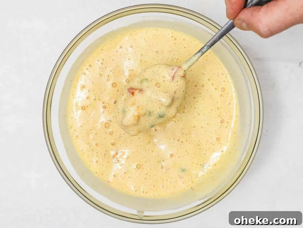 Savory Chickpea Frittata Muffins for Meal Prep 10 Chickpea Muffin batter with veggies and hand holding a spoon