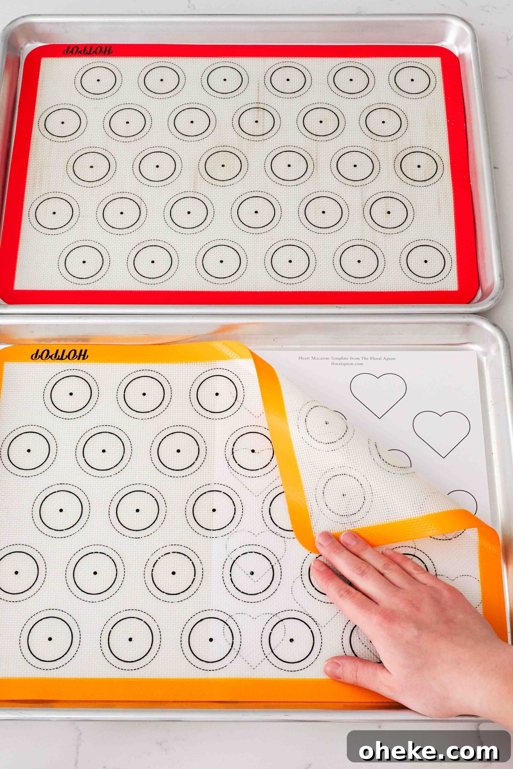 Heart-Shaped Chocolate Raspberry Macarons Recipe 10 Two baking sheets with silicone macaron mats and a paper template with hearts underneath.