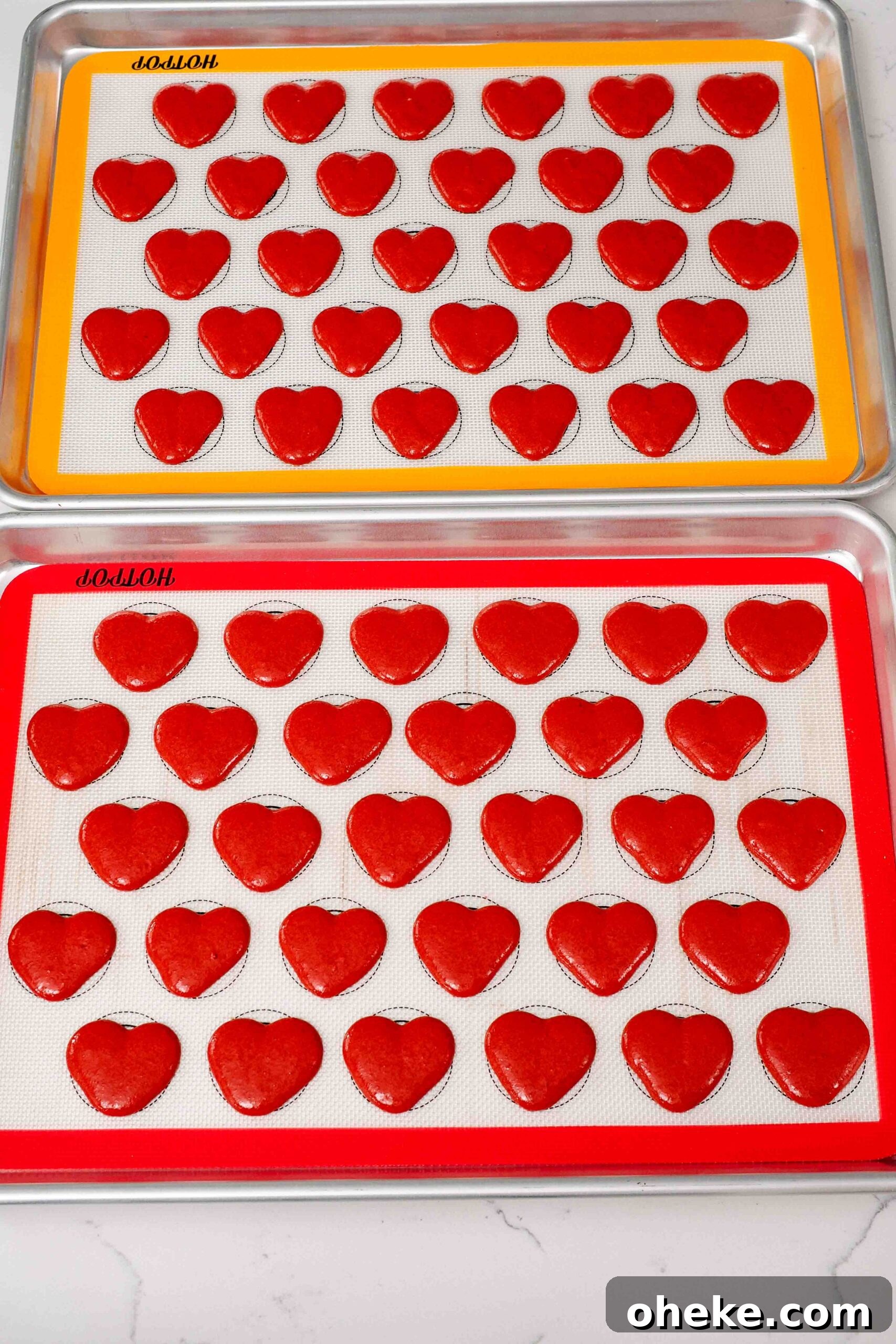 Heart-Shaped Chocolate Raspberry Macarons Recipe 13 Freshly piped heart macarons on silicone macaron mats.