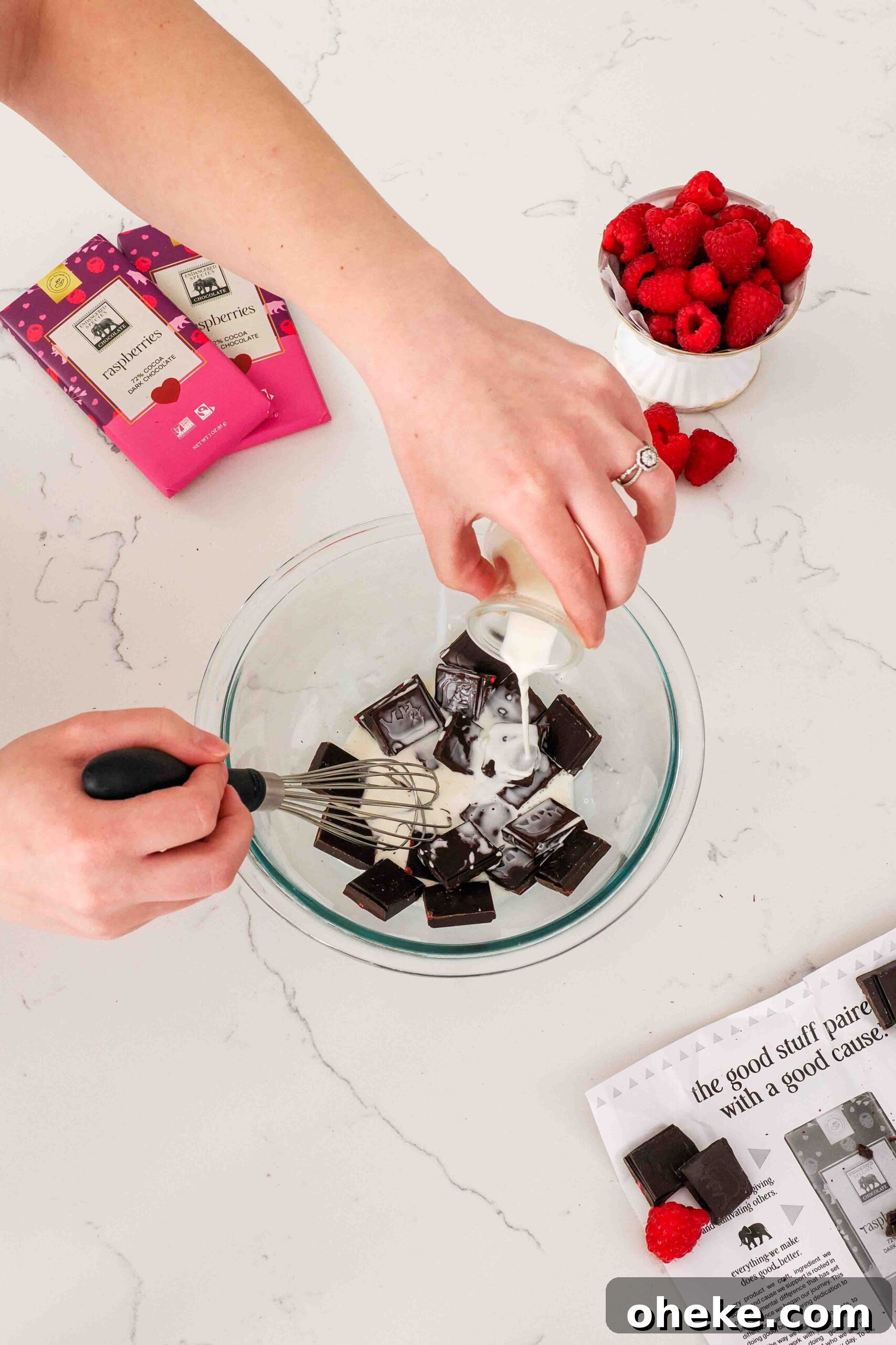 Heart-Shaped Chocolate Raspberry Macarons Recipe 15 A hand pours heavy cream into a bowl of pieces of raspberry chocolate.