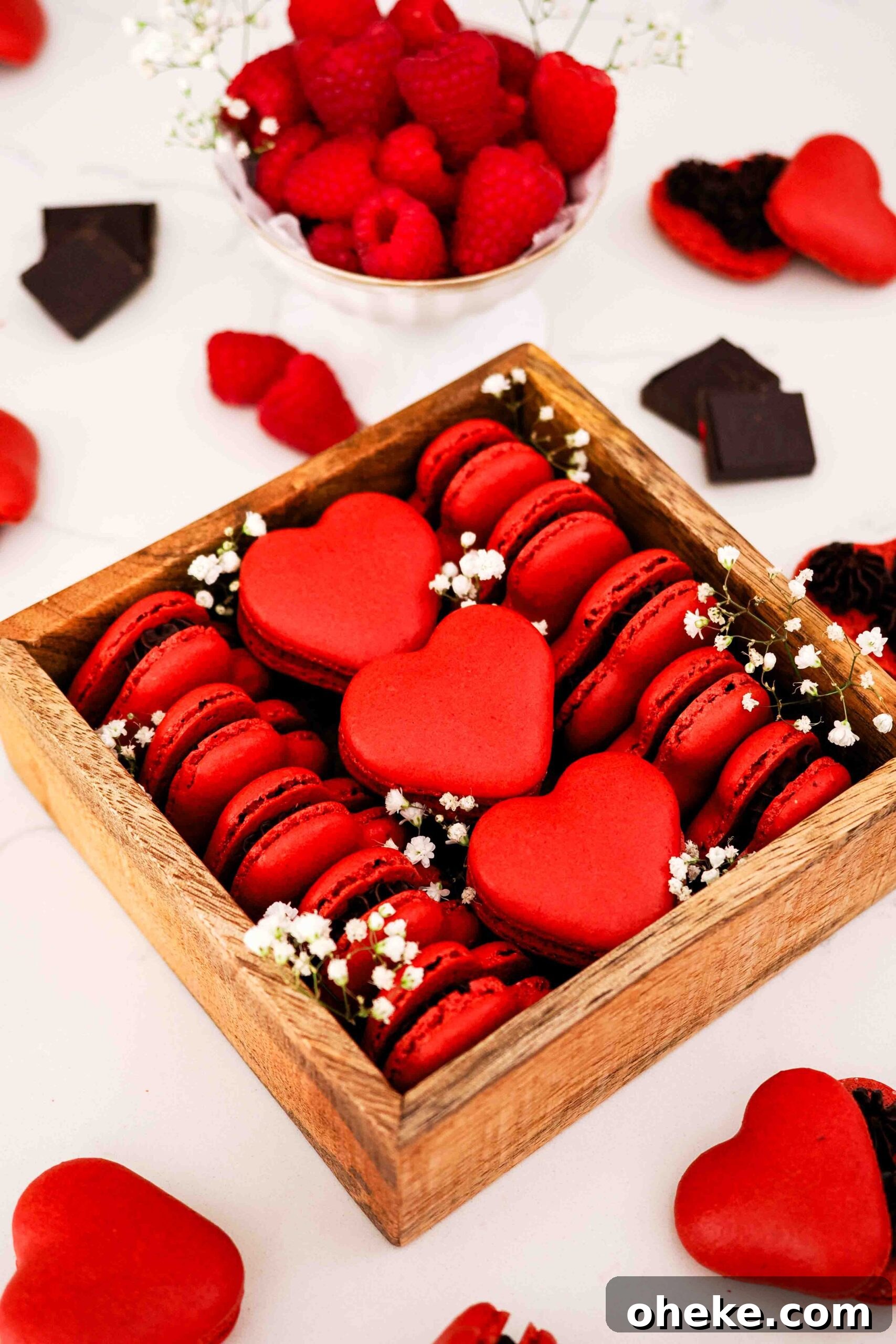 Heart-Shaped Chocolate Raspberry Macarons Recipe 18 A wooden box is filled with red, heart-shaped macarons and decorated with baby's breath flowers.