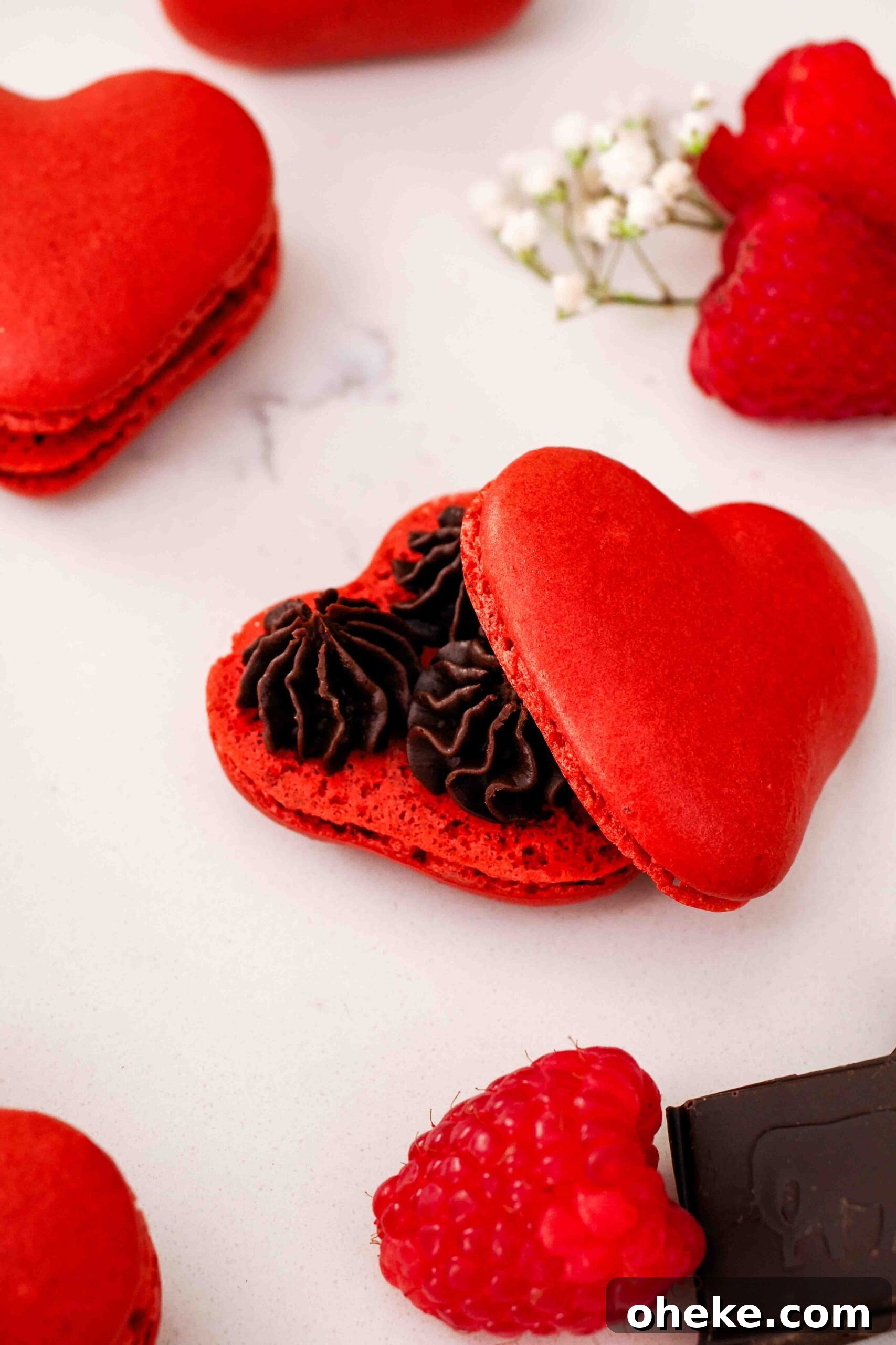 Heart-Shaped Chocolate Raspberry Macarons Recipe 3 A closeup of a single chocolate raspberry macaron, half open to see the ganache inside.