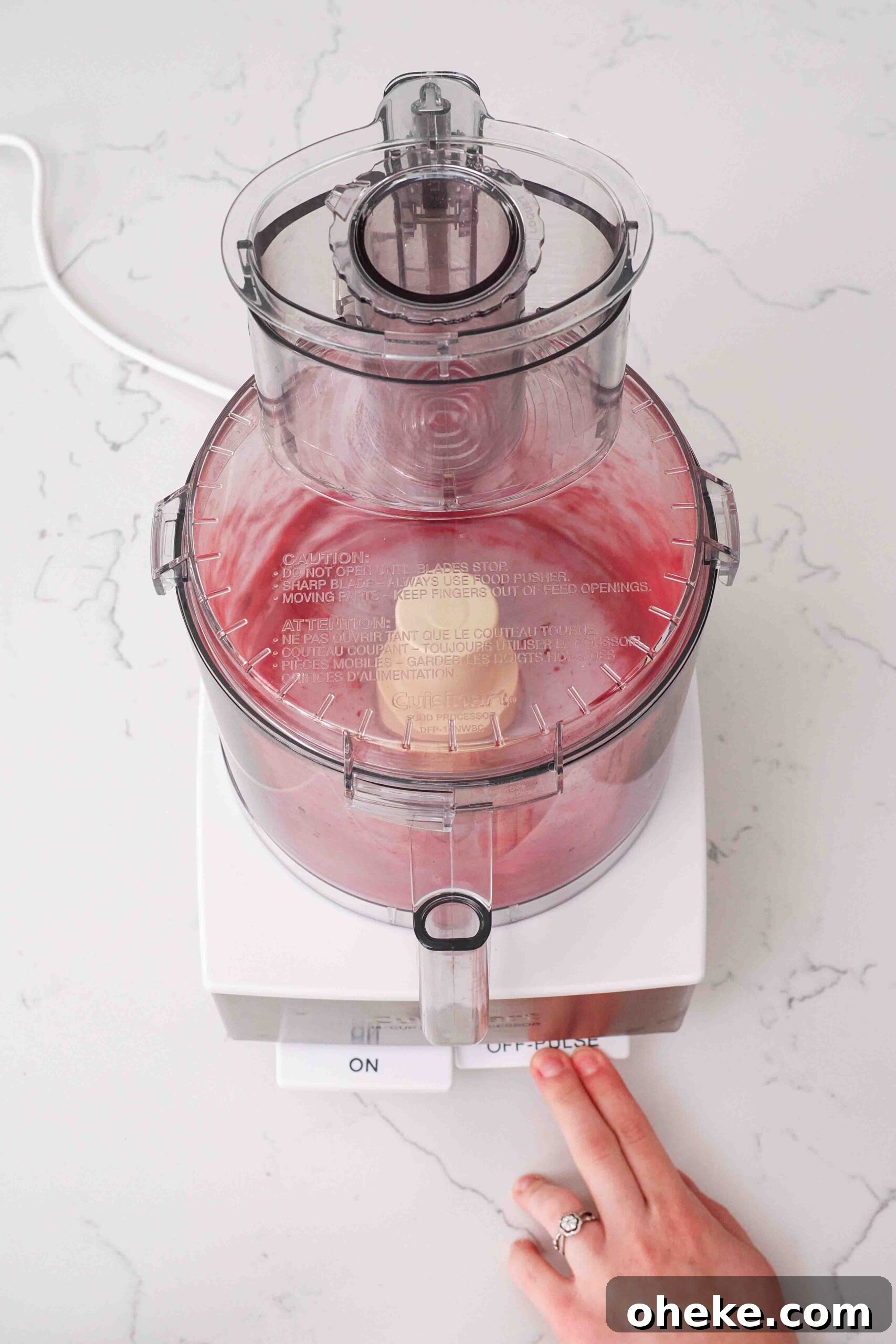 Heart-Shaped Chocolate Raspberry Macarons Recipe 4 A hand presses the "pulse" button on a food processor with freeze-dried raspberries.