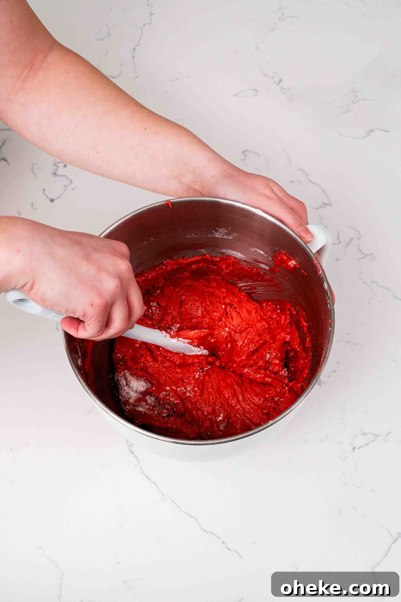 Heart-Shaped Chocolate Raspberry Macarons Recipe 8 Two hands fold macaron batter in a mixing bowl at the early stages, where it's still quite airy.