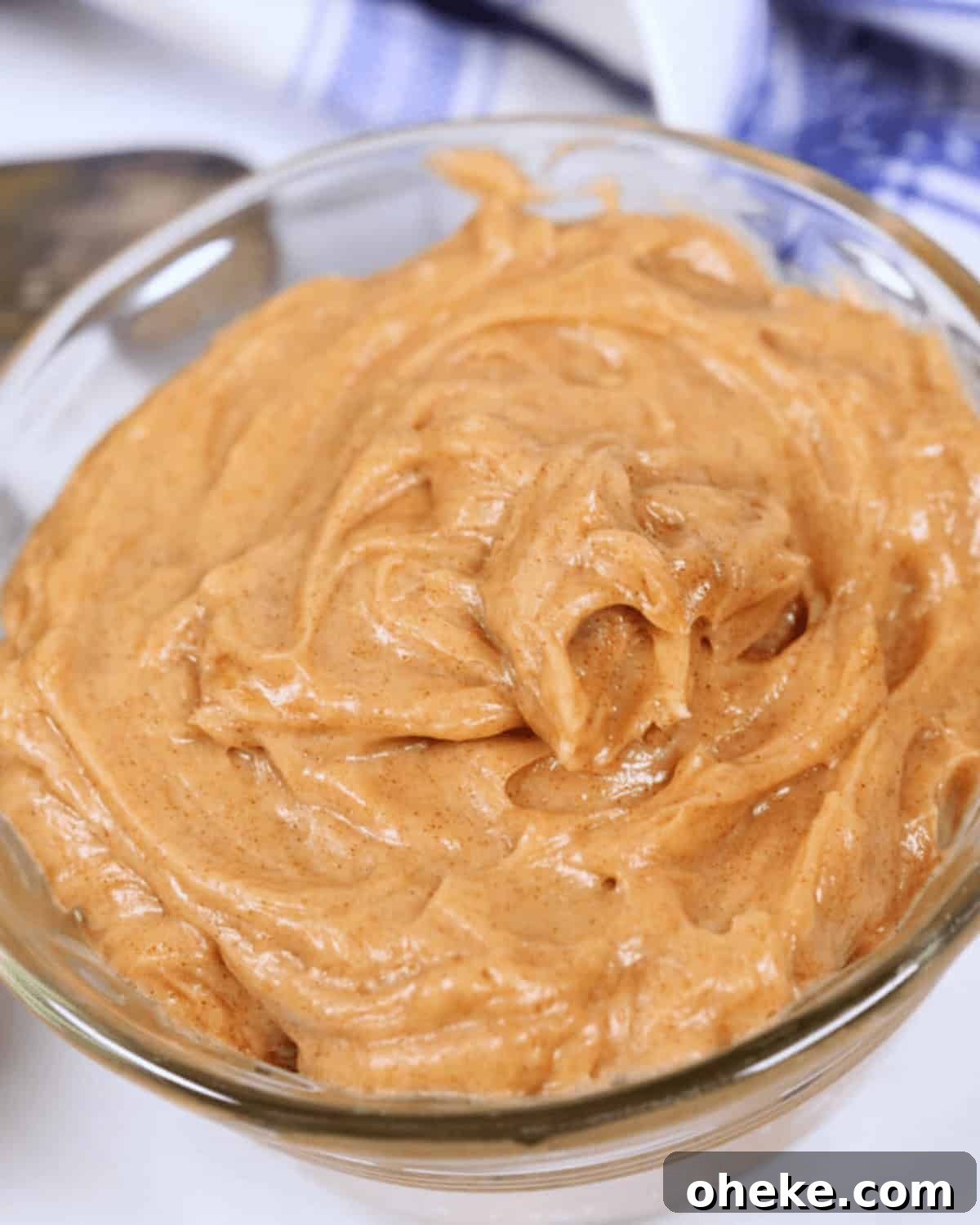 A close-up of a glass bowl filled with Texas Roadhouse Butter, with a spoon partially visible in the background.
