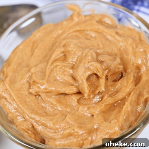 A close-up of a glass bowl filled with Texas Roadhouse Butter, with a spoon partially visible in the background.