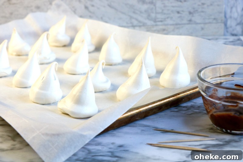 Ghost Meringues Recipe: How to Make Spooky Meringue Cookies 8 Perfectly made meringue ghosts drying on a parchment paper lined cookie sheet.