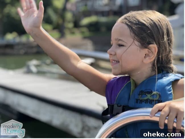 A girl waving while sitting on a dock by the water.