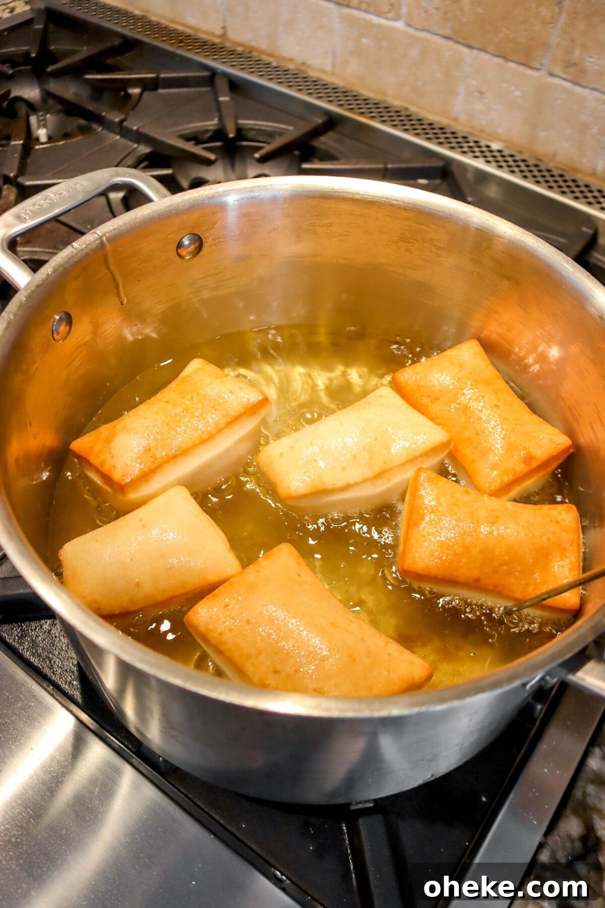 six golden brown beignets in pot of oil