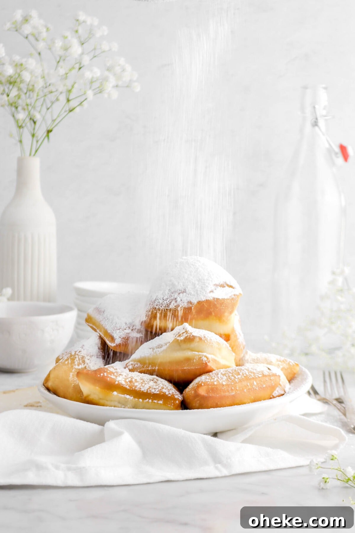 beignets in white bowl with powdered sugar dusting the tops with white napkin