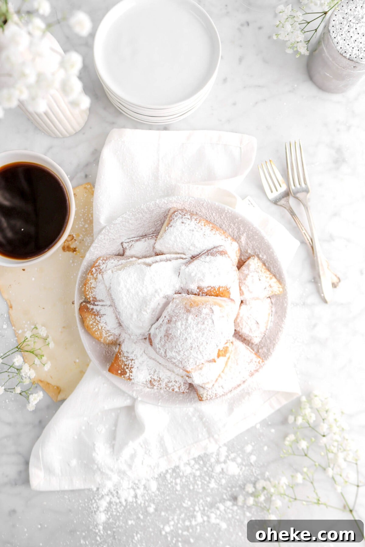 overhead shot of plate of beignets on white napkin with flowers and cup of coffee