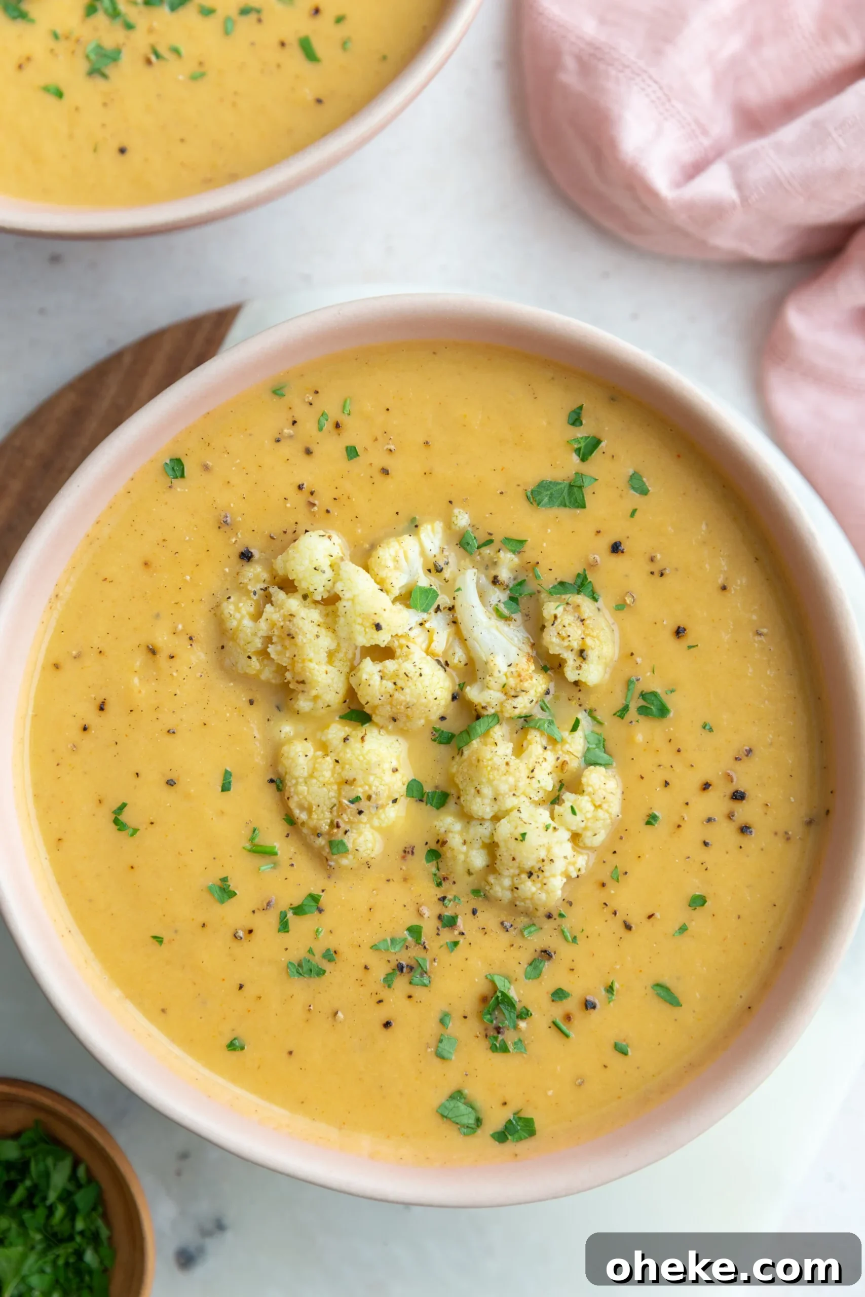 Roasted Cauliflower Soup with Garlic and Parmesan 2 big pink bowl filled with orange cauliflower soup topped with roasted cauliflower and fresh herbs