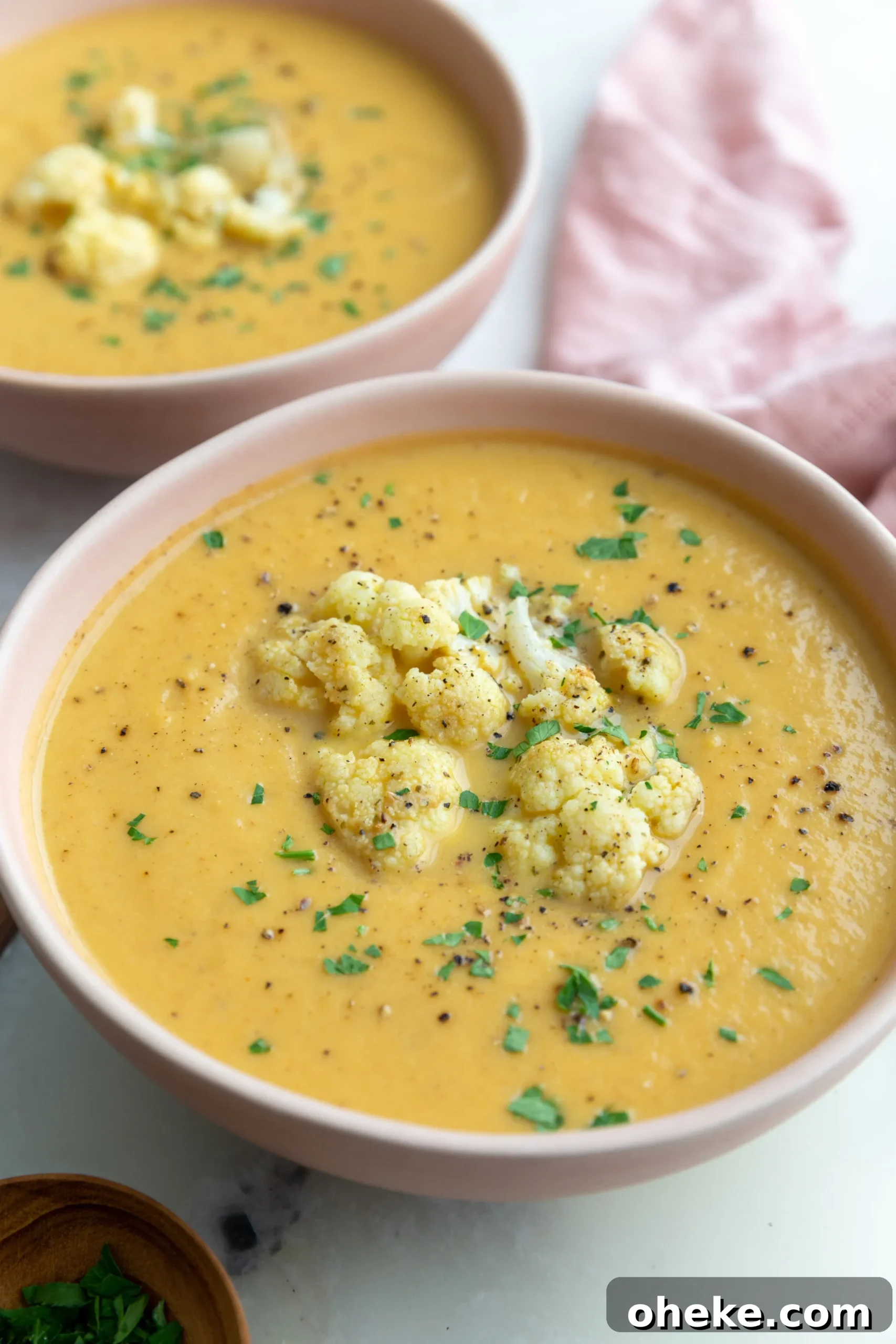 Roasted Cauliflower Soup with Garlic and Parmesan 3 big pink bowl filled with orange cauliflower soup topped with roasted cauliflower and fresh herbs
