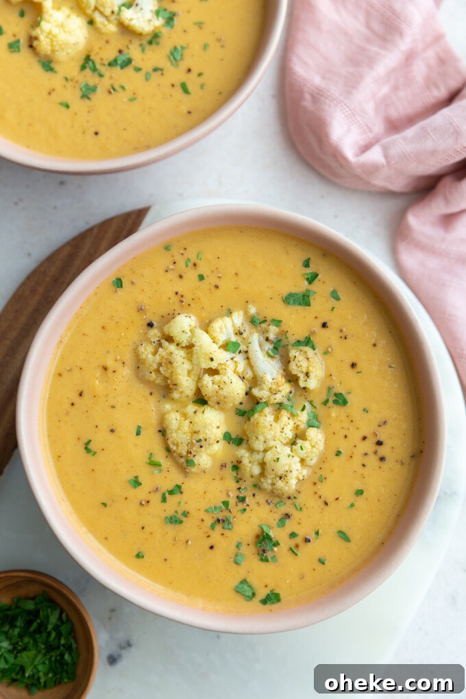 Roasted Cauliflower Soup with Garlic and Parmesan 4 big pink bowl filled with orange cauliflower soup topped with roasted cauliflower and fresh herbs