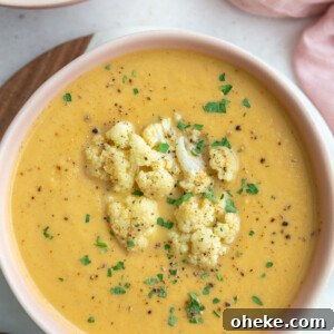 Roasted Cauliflower Soup with Garlic and Parmesan 7 big pink bowl filled with orange cauliflower soup topped with roasted cauliflower and fresh herbs