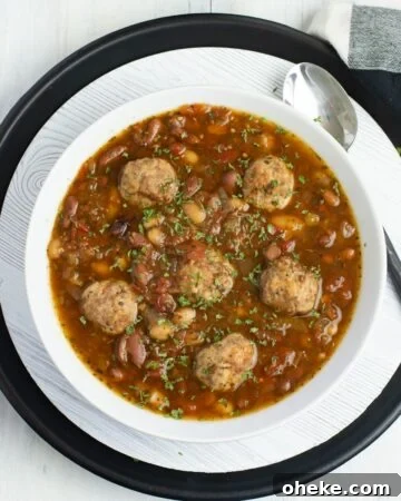 A white bowl filled with Italian Bean Meatball Soup.