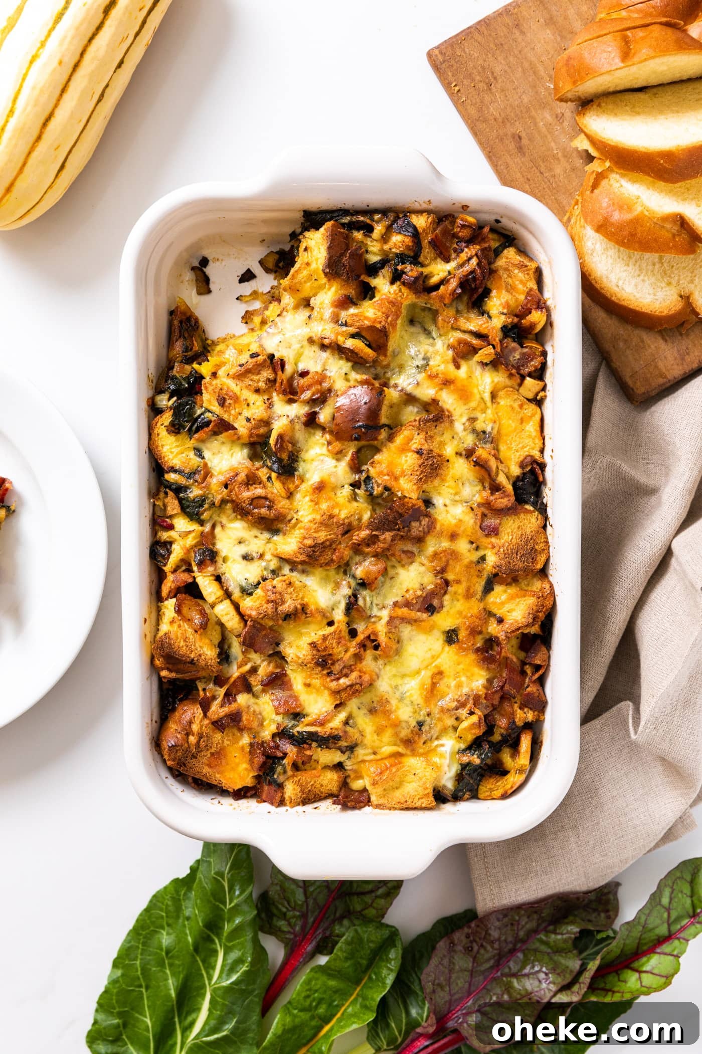 Top down view of white casserole dish sitting on white countertop filled with brown colored egg strata with slices of bread on the side