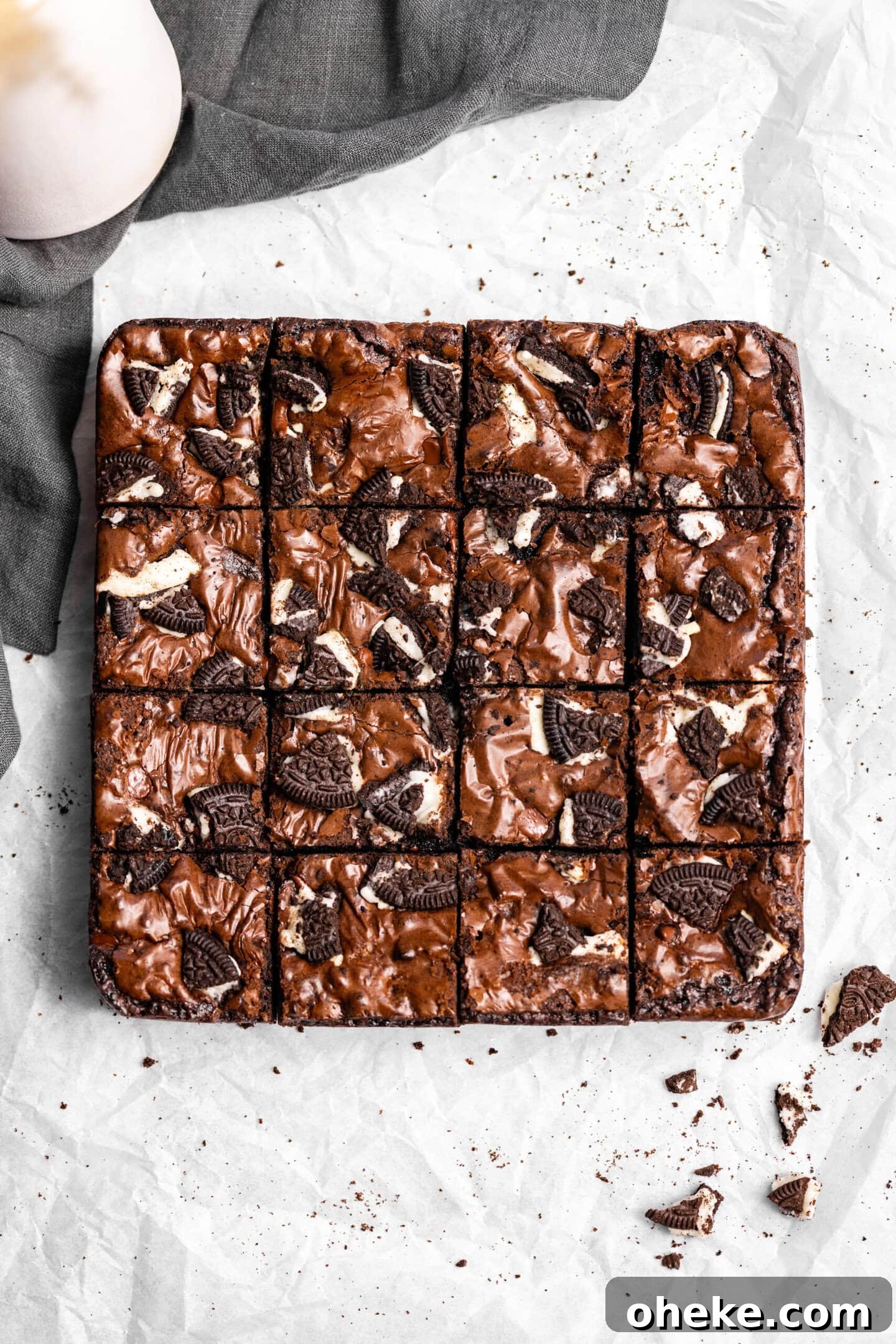 Oreo Brownies on top of parchment paper with pieces of Oreo cookies and a glass of milk and napkin nearby.