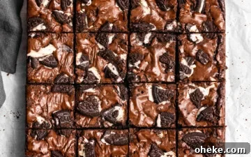 Oreo Brownies on top of parchment paper with pieces of Oreo cookies and a glass of milk and napkin nearby.