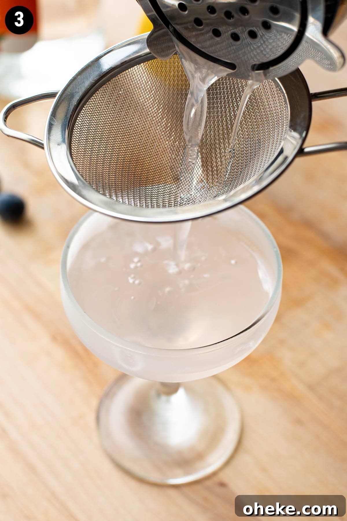 Blueberry Martini Recipe: How to Make a Refreshing Blueberry Cocktail 5 Double straining a blueberry martini into a chilled coupe glass.